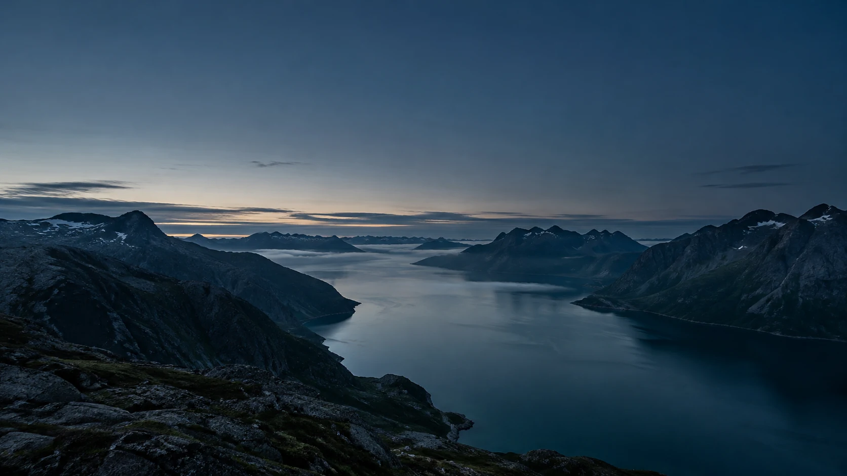 A quiet Nordic fjord with dark teal water between mountains at blue hour.